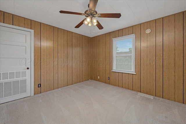 spare room with a ceiling fan, carpet flooring, wood walls, and visible vents