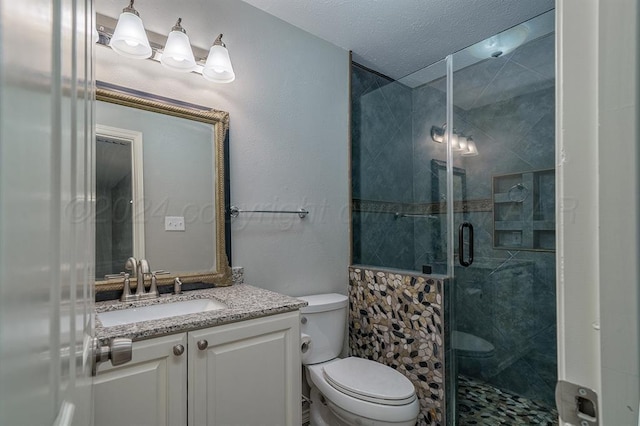 bathroom with a textured ceiling, vanity, toilet, and a shower with shower door