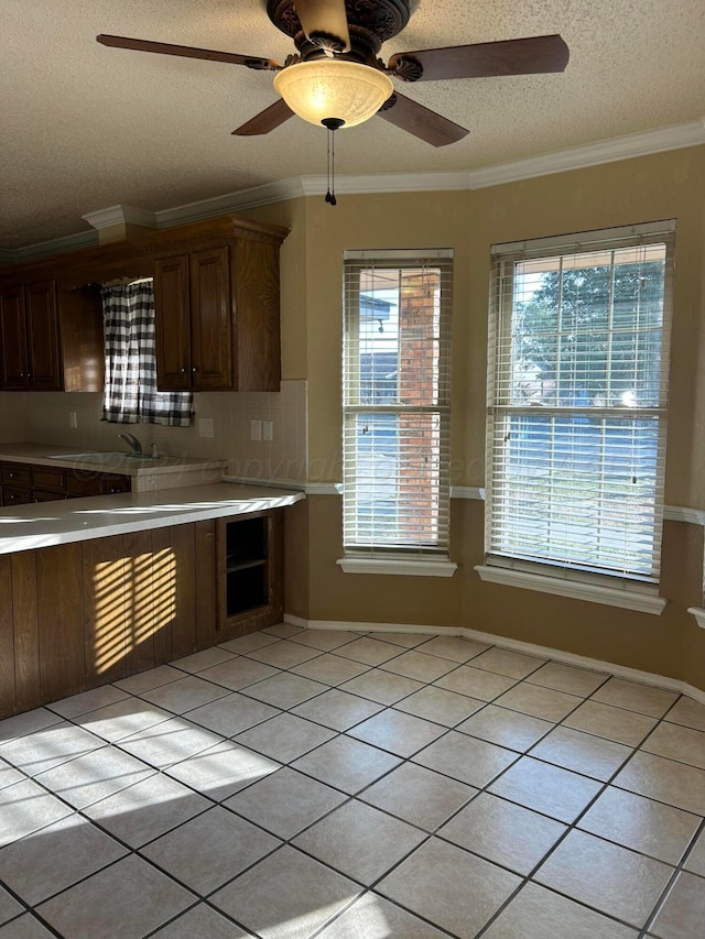 kitchen with backsplash, crown molding, light countertops, light tile patterned floors, and a textured ceiling