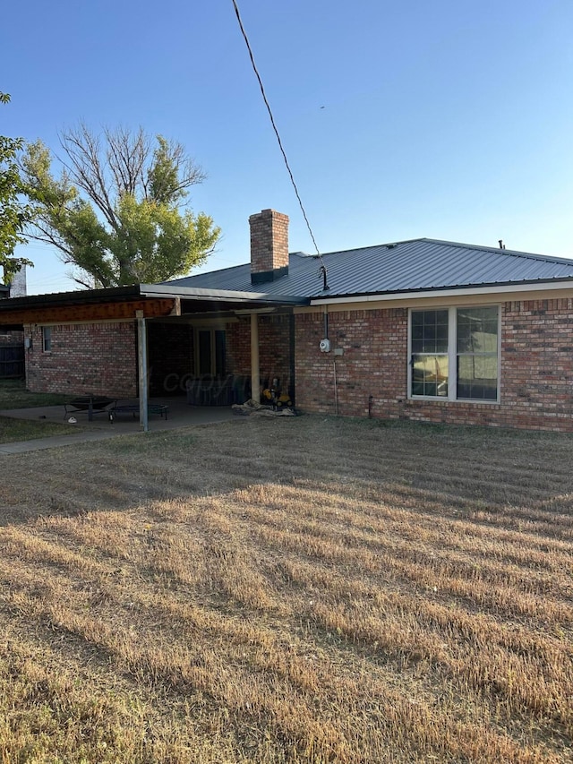 rear view of house with brick siding, a chimney, a yard, and metal roof