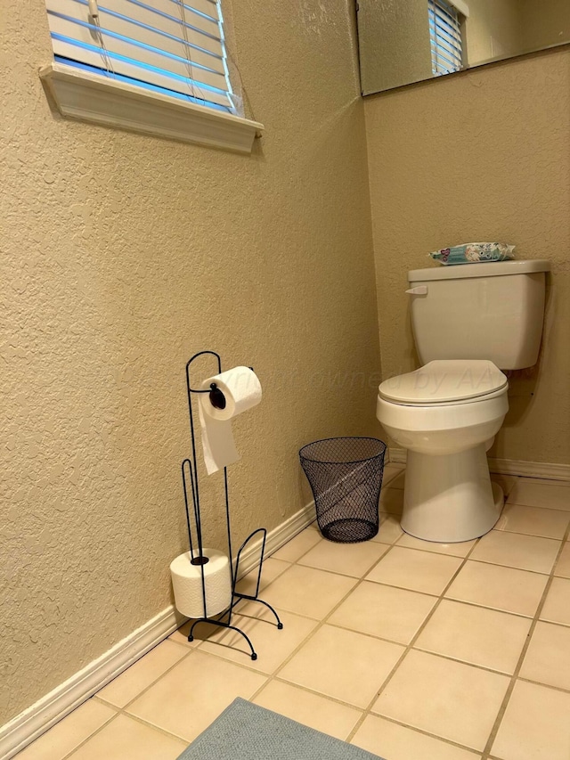 half bath featuring tile patterned floors, toilet, a textured wall, and baseboards