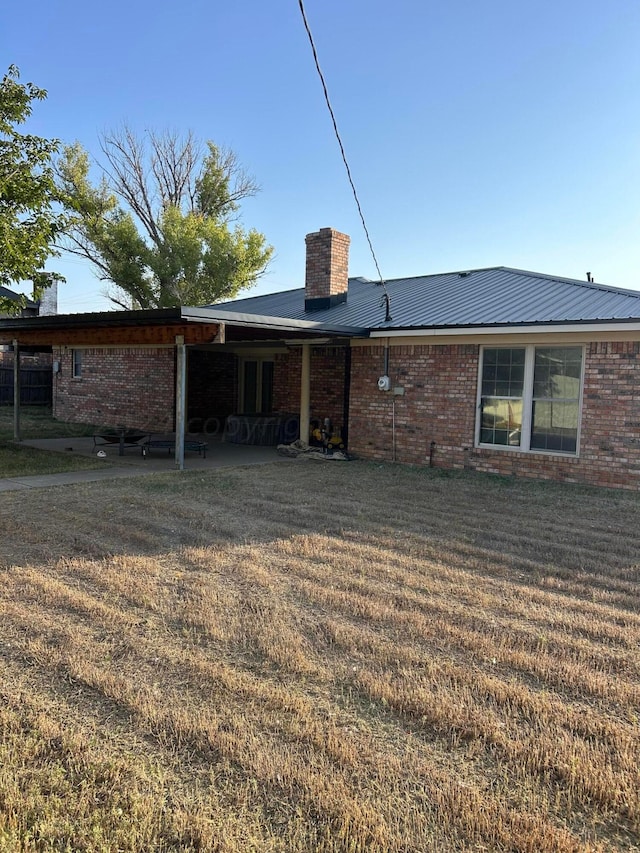 back of house featuring a yard, brick siding, metal roof, and a chimney