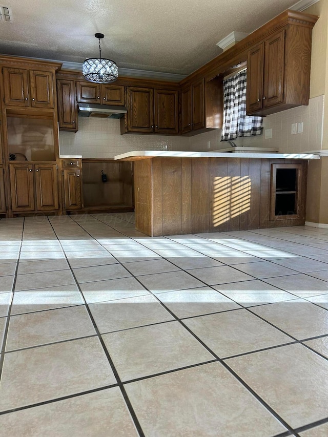 kitchen with light tile patterned floors, tasteful backsplash, under cabinet range hood, and ornamental molding