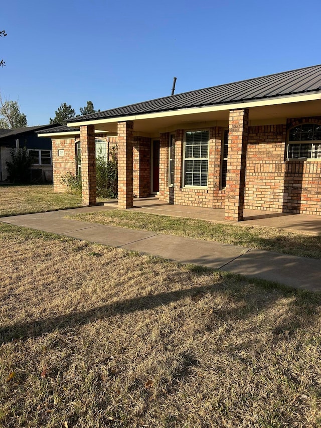 view of front of house featuring metal roof, brick siding, and a front lawn