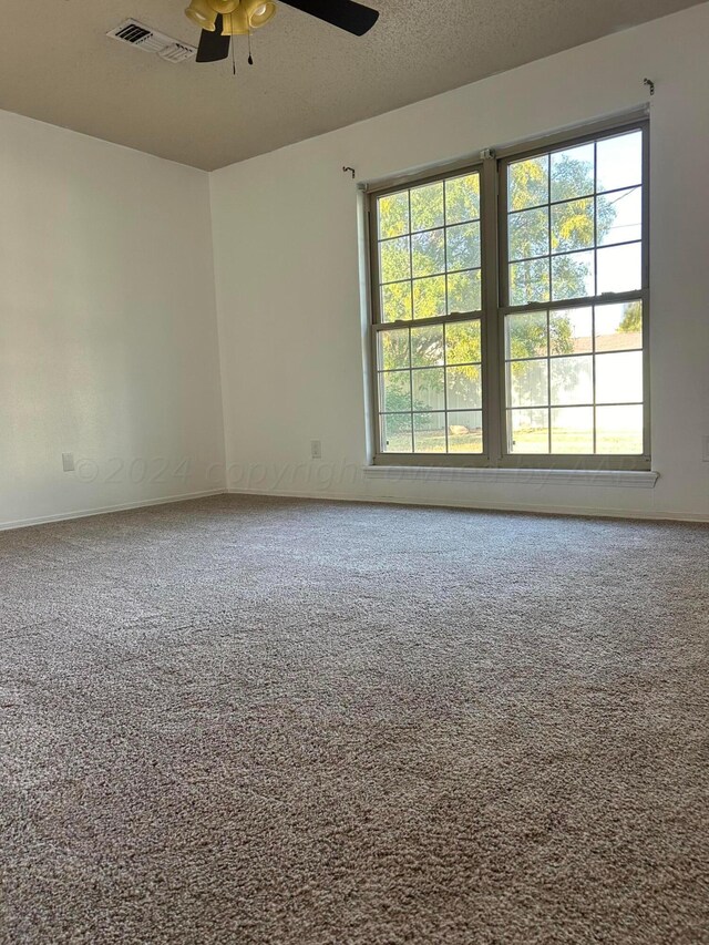 carpeted empty room featuring plenty of natural light, visible vents, and ceiling fan