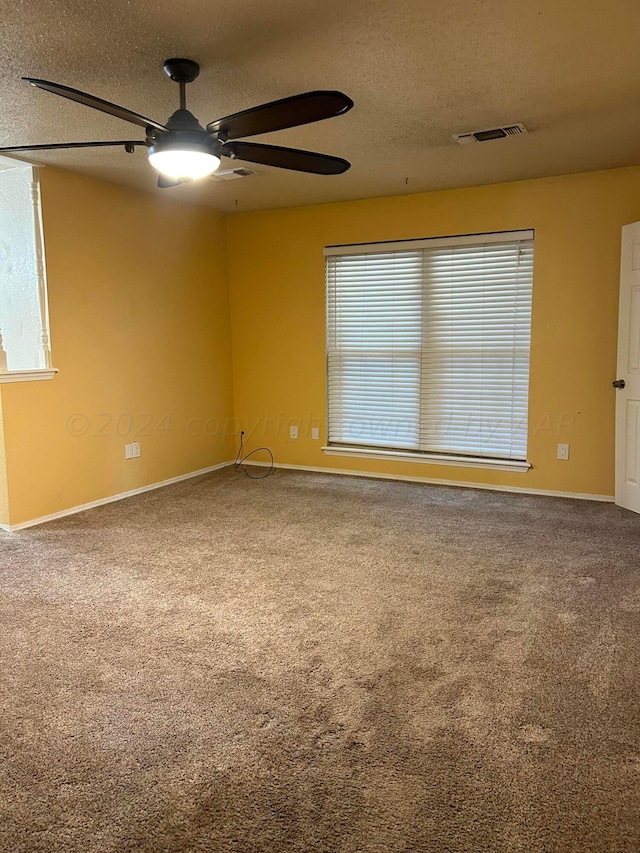 empty room featuring carpet, baseboards, visible vents, ceiling fan, and a textured ceiling