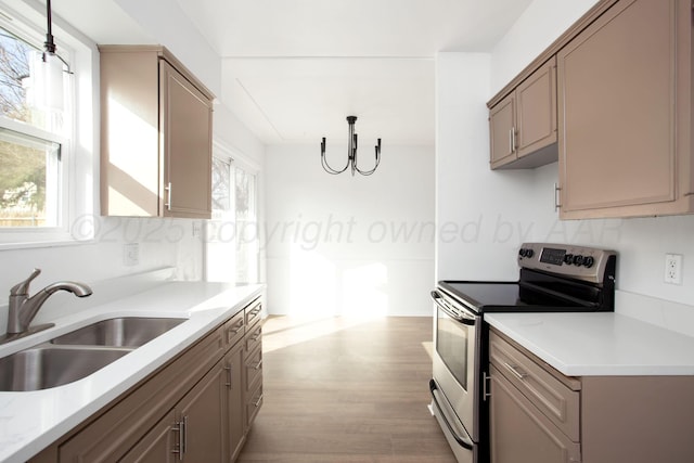 kitchen with sink, an inviting chandelier, stainless steel electric range oven, hanging light fixtures, and light hardwood / wood-style flooring