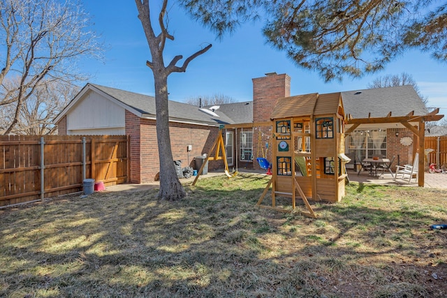 rear view of house featuring brick siding, a fenced backyard, a chimney, a patio area, and a playground