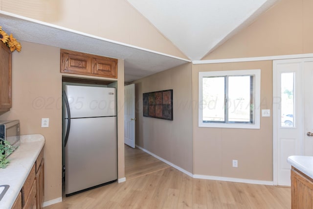 233 Doucette Dr, Howardwick, TX 79226 - kitchen with stainless steel appliances, light wood-style floors, brown cabinetry, light countertops, and vaulted ceiling