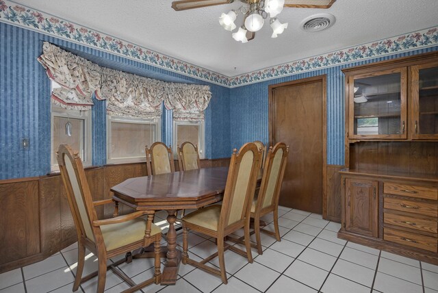 6814 Blacksmith Ln, Amarillo, TX 79109 - dining room featuring wallpapered walls, ceiling fan, a textured ceiling, light tile patterned floors, and a wainscoted wall
