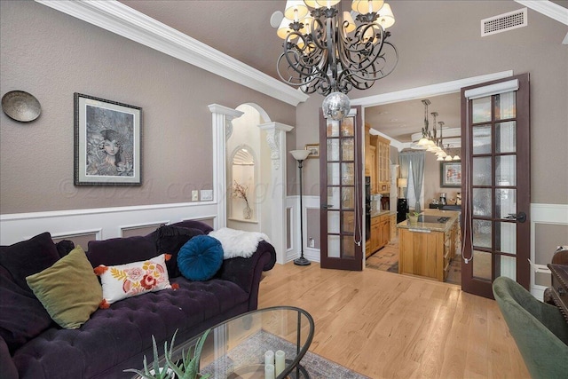 living room featuring hardwood / wood-style floors, ornamental molding, french doors, and a chandelier