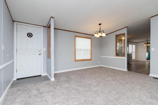 foyer with a chandelier, dark colored carpet, and crown molding