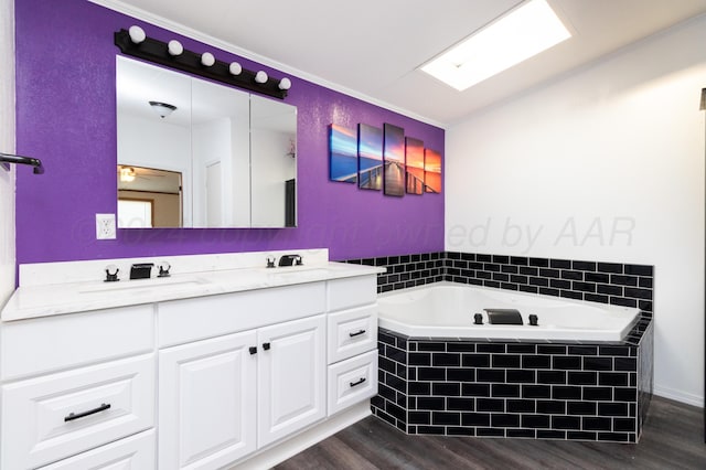 bathroom with tiled bath, vanity, hardwood / wood-style flooring, and ceiling fan