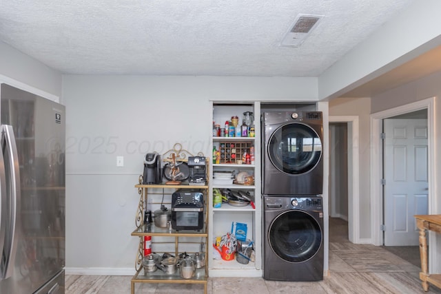 laundry area featuring baseboards, stacked washing maching and dryer, a textured ceiling, visible vents, and laundry area