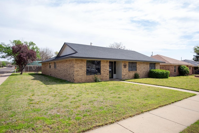 ranch-style home with brick siding, a front yard, and roof with shingles
