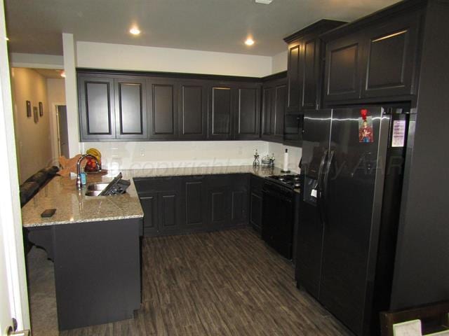 kitchen with a kitchen bar, sink, light stone counters, kitchen peninsula, and black appliances