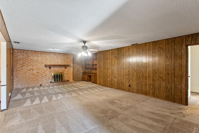 unfurnished living room with ceiling fan, light carpet, a textured ceiling, wooden walls, and a fireplace