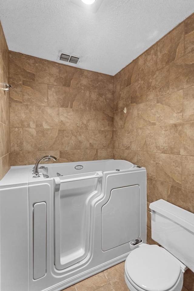 bathroom featuring tile patterned floors, a tub to relax in, toilet, and a textured ceiling