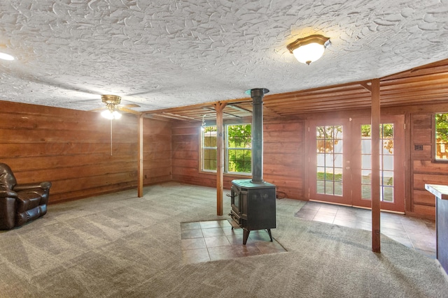 carpeted living room featuring a wood stove, ceiling fan, and wood walls