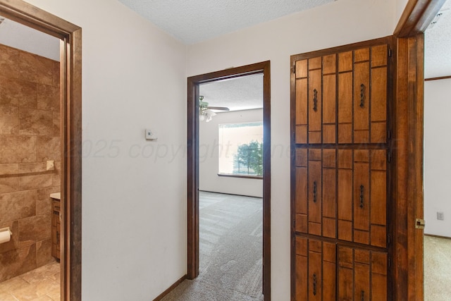 hall with a textured ceiling and light colored carpet