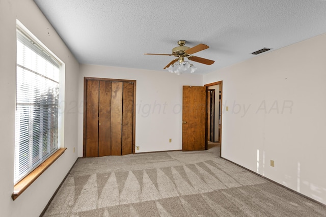 unfurnished bedroom with a textured ceiling, ceiling fan, light carpet, and a closet