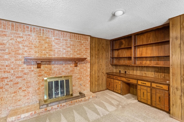 unfurnished office with light carpet, a brick fireplace, a textured ceiling, built in desk, and wood walls