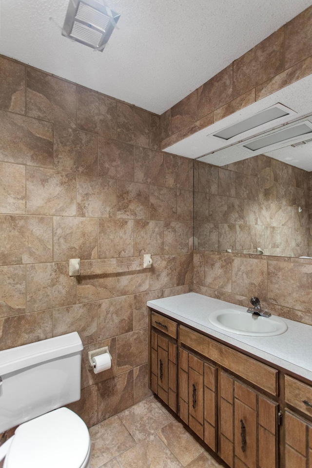 bathroom with a textured ceiling, vanity, tile walls, and toilet