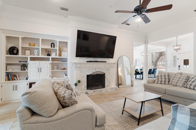 living area featuring light wood finished floors, visible vents, a high end fireplace, ornamental molding, and ceiling fan with notable chandelier