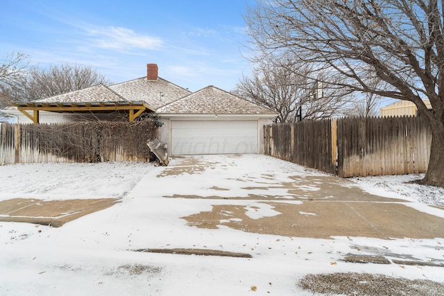 view of snow covered exterior with a garage, fence, and a chimney