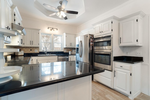 kitchen featuring stainless steel appliances, a sink, white cabinetry, dark countertops, and a raised ceiling