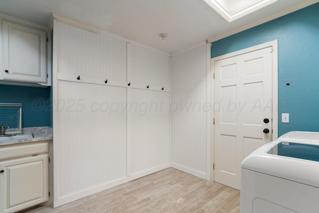 clothes washing area featuring washer / clothes dryer, cabinet space, light wood-style flooring, ornamental molding, and a sink