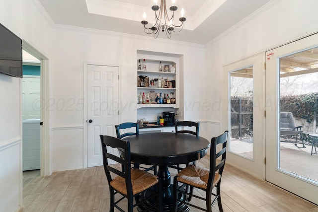 dining space with a chandelier, a tray ceiling, ornamental molding, and light wood-style flooring