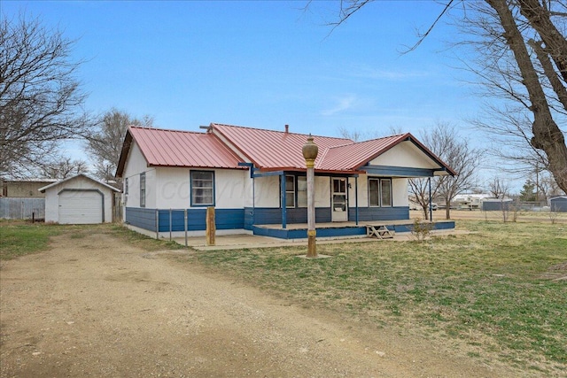 view of front of property featuring an outbuilding, metal roof, a detached garage, fence, and driveway