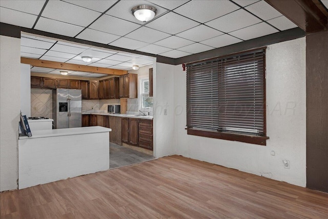 kitchen with a paneled ceiling, a sink, light countertops, stainless steel refrigerator with ice dispenser, and light wood finished floors