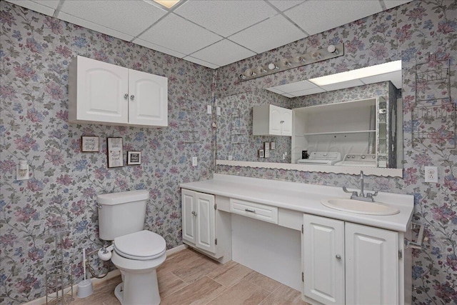 bathroom featuring toilet, vanity, washer and dryer, a drop ceiling, and wallpapered walls