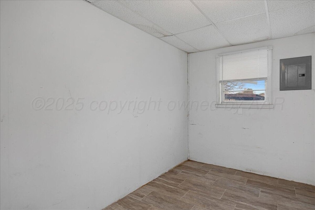 empty room featuring electric panel, a drop ceiling, and wood finished floors