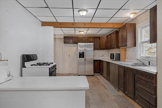 kitchen with tasteful backsplash, appliances with stainless steel finishes, light countertops, dark brown cabinets, and a sink