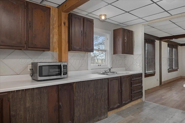 kitchen with a drop ceiling, a sink, light countertops, decorative backsplash, and stainless steel microwave