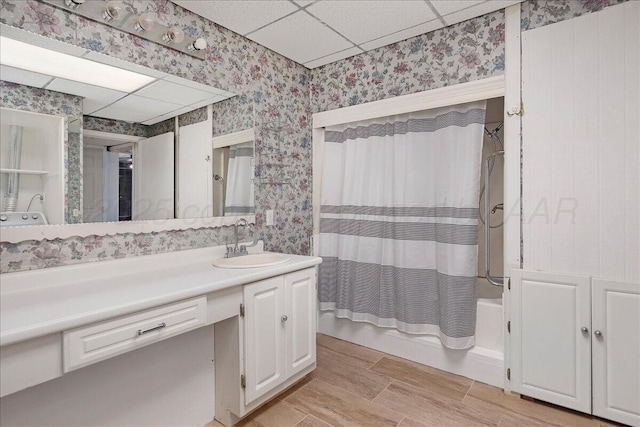 bathroom with a drop ceiling, shower / bath combination with curtain, vanity, and wallpapered walls