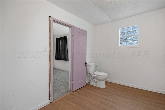 bathroom with a textured ceiling, wood finished floors, toilet, and baseboards