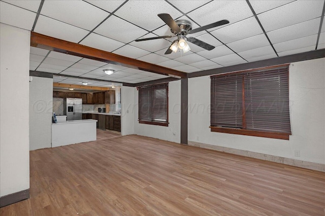 unfurnished living room featuring light wood finished floors, a drop ceiling, a ceiling fan, and baseboards