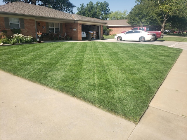 view of green lawn featuring a garage and concrete driveway