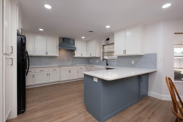 kitchen featuring light hardwood / wood-style flooring, white cabinetry, kitchen peninsula, and wall chimney exhaust hood