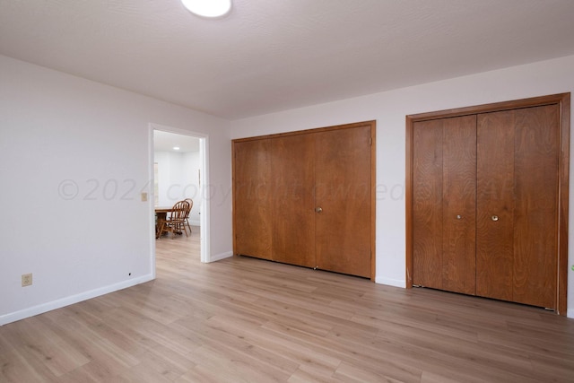 unfurnished bedroom featuring light wood-type flooring and two closets