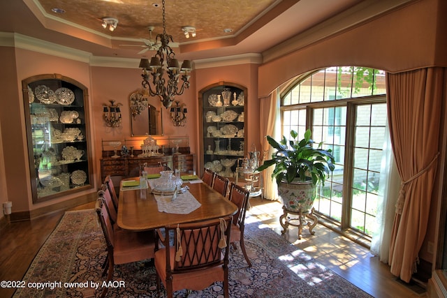 dining area with wood-type flooring, built in shelves, a chandelier, crown molding, and a tray ceiling