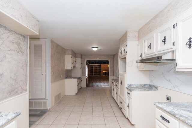 2709 Mohawk Dr, Amarillo, TX 79109 - kitchen with light tile patterned flooring, white cabinets, under cabinet range hood, a wainscoted wall, and light stone countertops