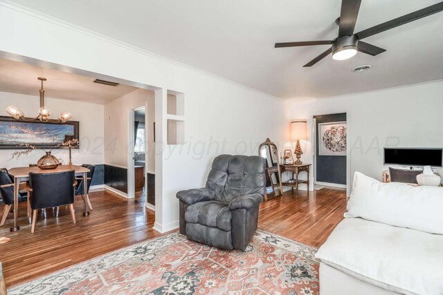 living room with wood-type flooring, crown molding, and ceiling fan with notable chandelier