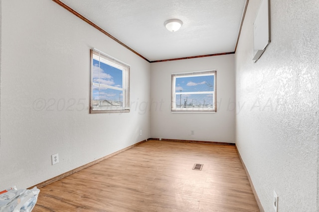 empty room featuring light wood-type flooring, visible vents, crown molding, and a textured wall