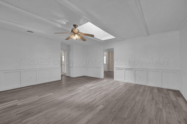spare room with a textured ceiling, a ceiling fan, a skylight, a decorative wall, and wood finished floors