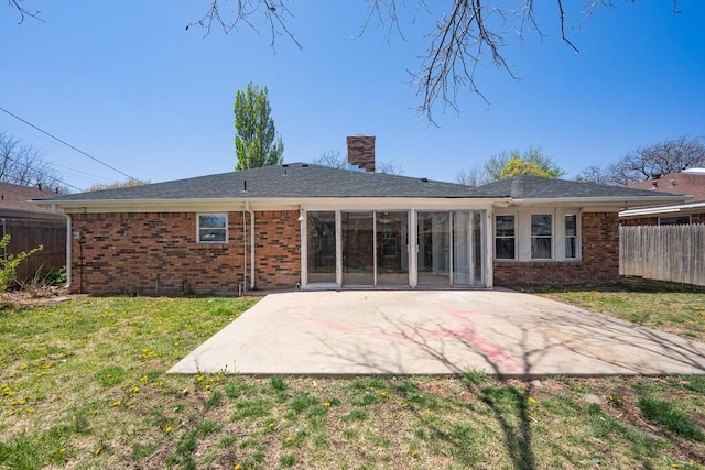 back of property with a patio, a chimney, brick siding, fence, and a lawn